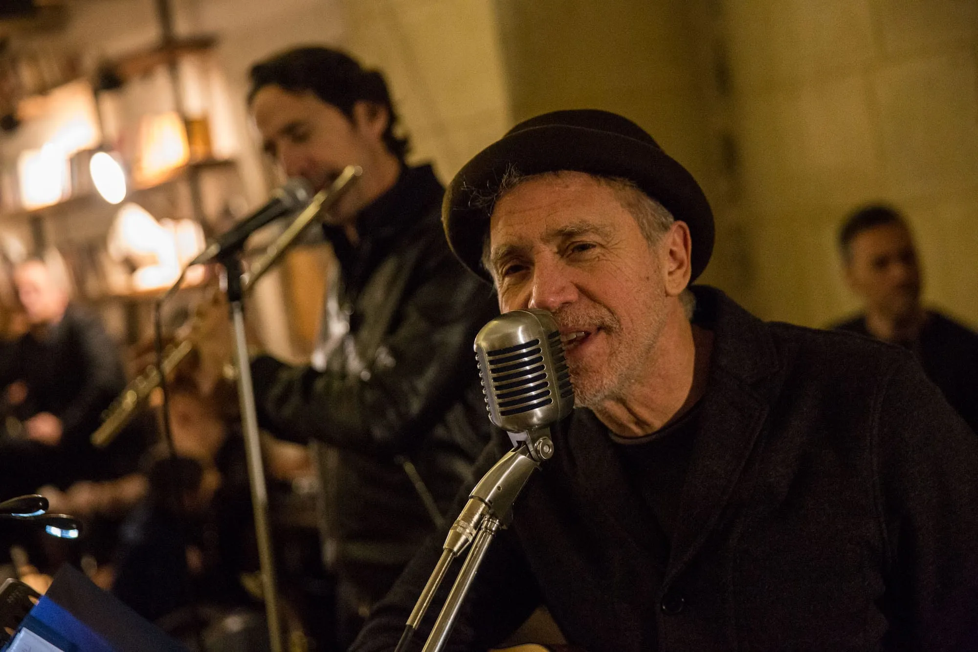 Una serata di musica dal vivo nel salone: il cantante col cappello al microfono d’epoca, dietro di lui il chitarrista.