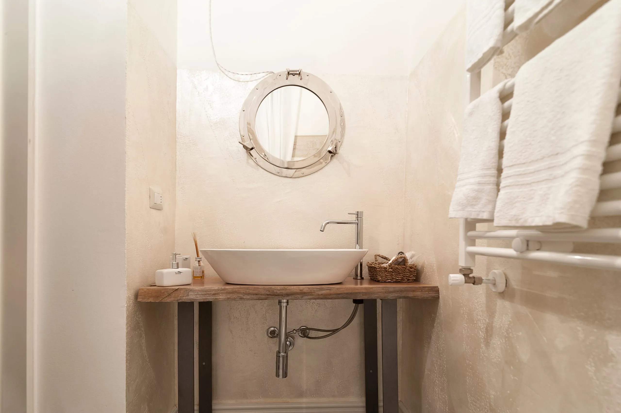 Il lavabo della suite Ascilò su una mensola di legno grezzo e, al posto dello specchio, un oblò di nave in ottone.