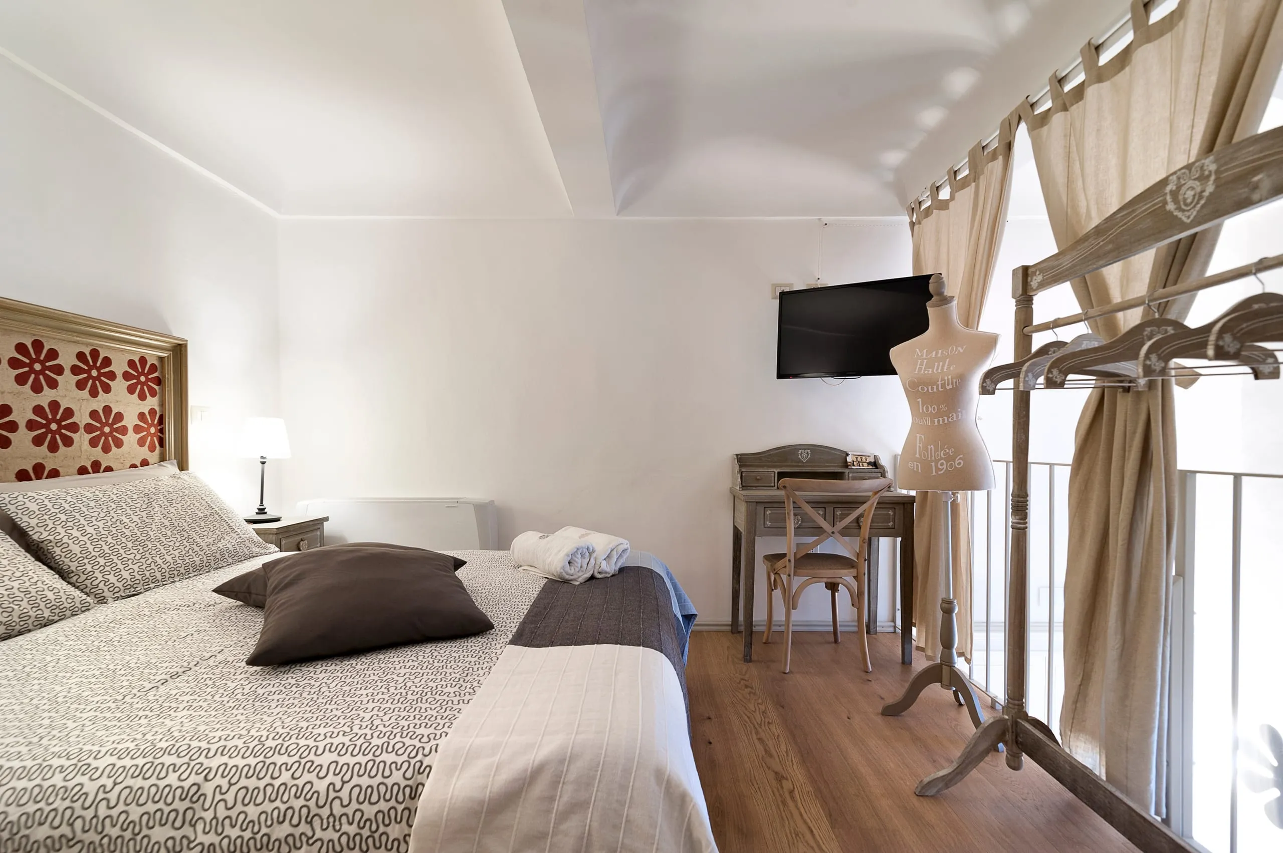 La camera di Casa Grika: il letto con la testiera a fiori rossi, il soppalco col parapetto in legno, un manichino da sartoria e lo scrittoio sotto la televisione.