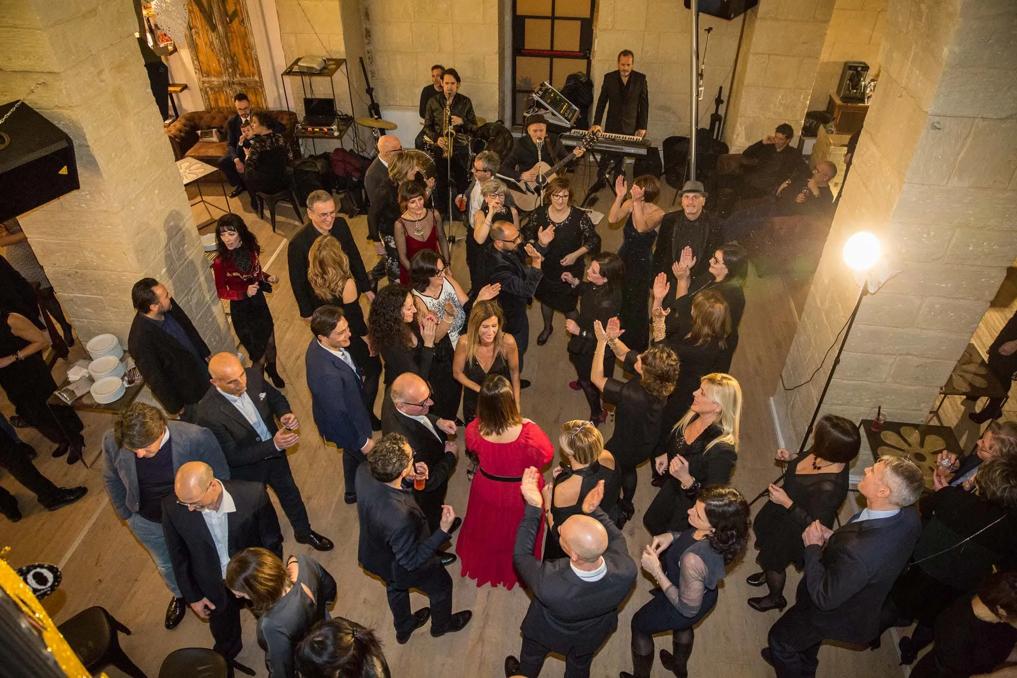 Una festa nel salone vista dall’alto: gli invitati ballano fra le colonne di pietra, la band sul fondo.
