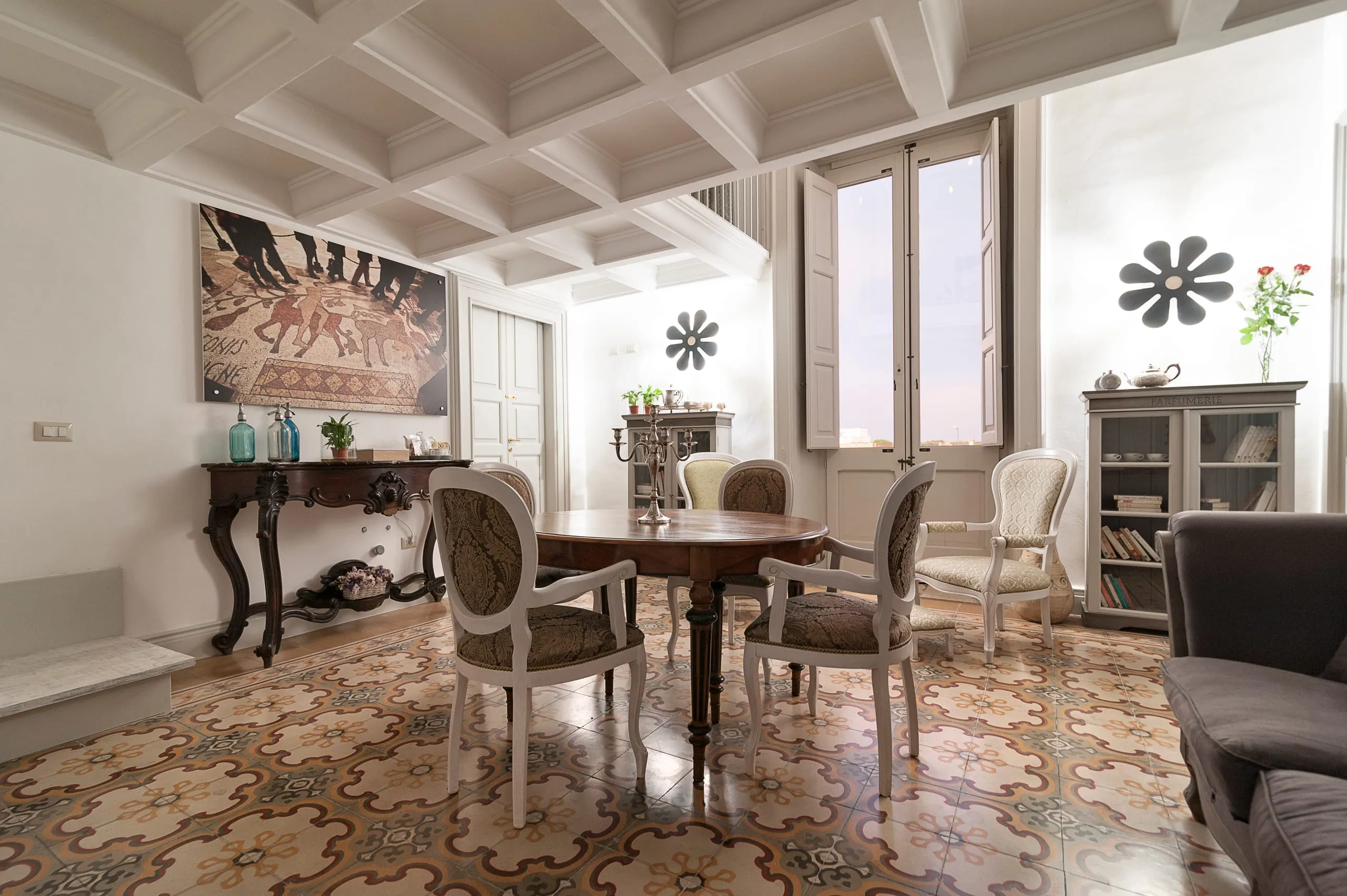 La suite Flora: il grande mosaico romano sopra la consolle intagliata, il tavolo con le sedie imbottite, le appliques a fiore e la portafinestra sul balcone.