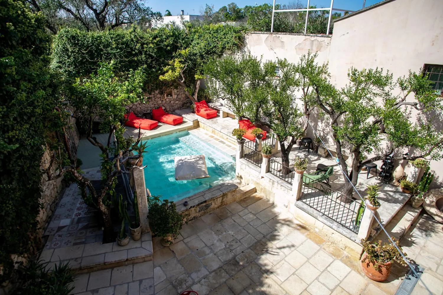 Il giardino di Palazzo Mandurino: la piccola piscina fra gli ulivi, i lettini rossi e la pavimentazione in pietra.