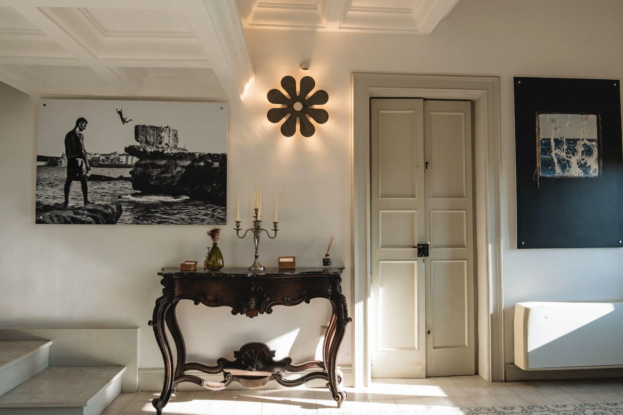 L’ingresso di Palazzo Mandurino: una consolle intagliata sotto il soffitto a cassettoni, il candelabro d’argento e l’applique a fiore accesa sulla parete.