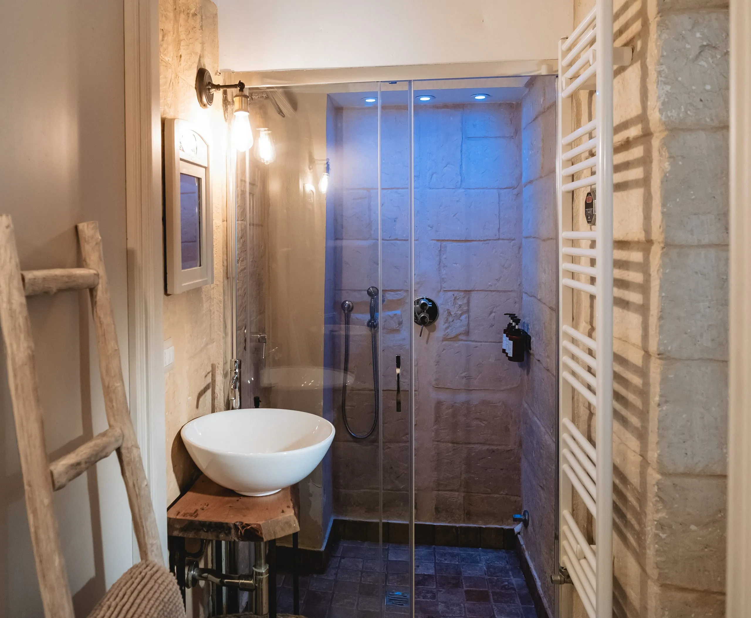 Il bagno di Lu Rusciu te lu Mare: il lavabo in ceramica, una scala di legno appendiabiti e il bagno turco in pietra dietro il vetro.