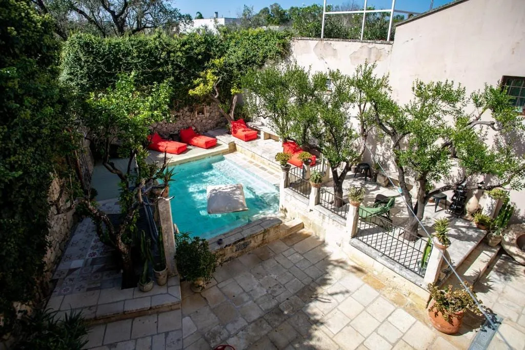 Il giardino visto dall’alto: la piccola piscina fra gli ulivi, i cuscinoni rossi e le terrazze in pietra.