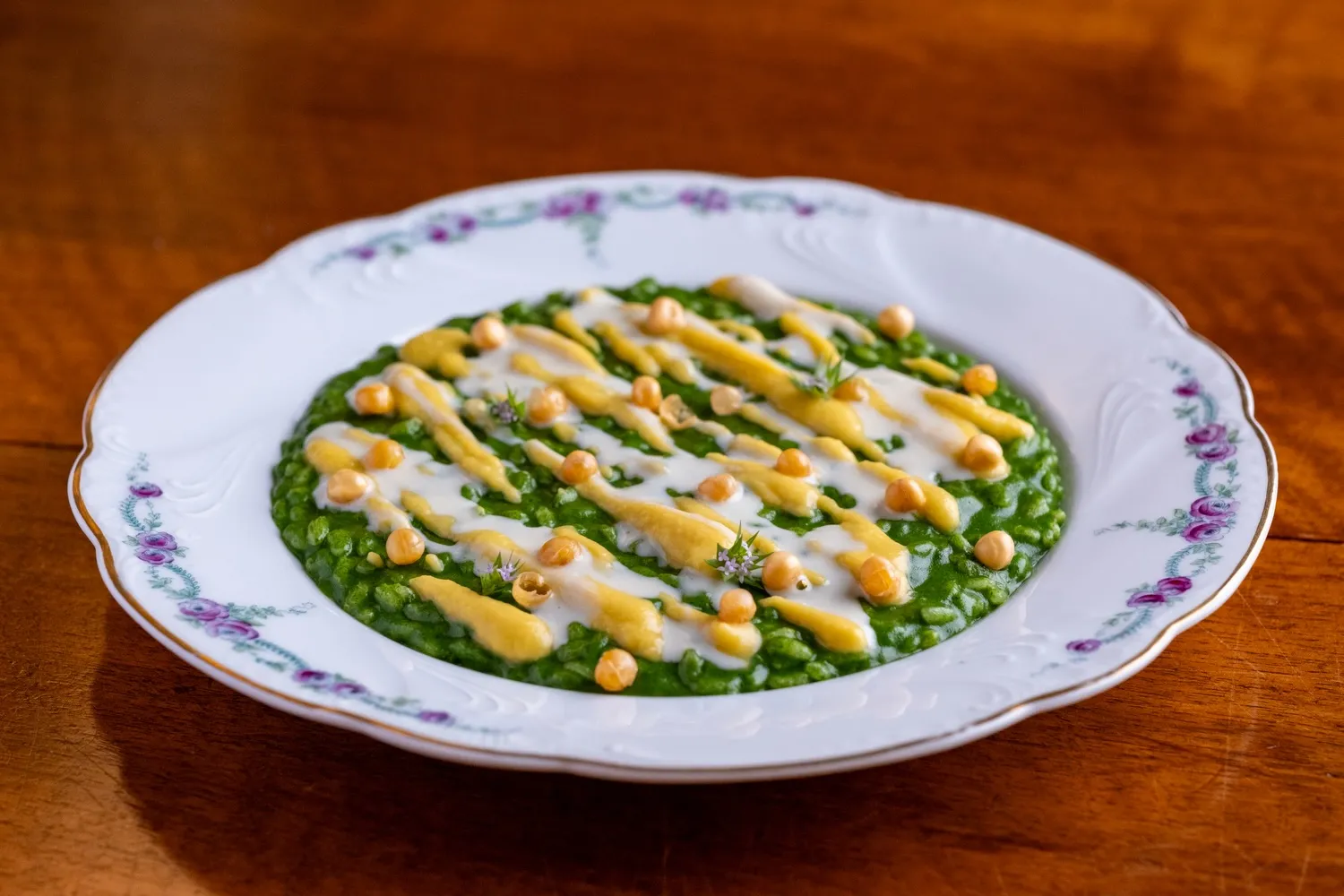 Un risotto alle erbe con ceci e crema, servito su un piatto d’epoca decorato a rose.