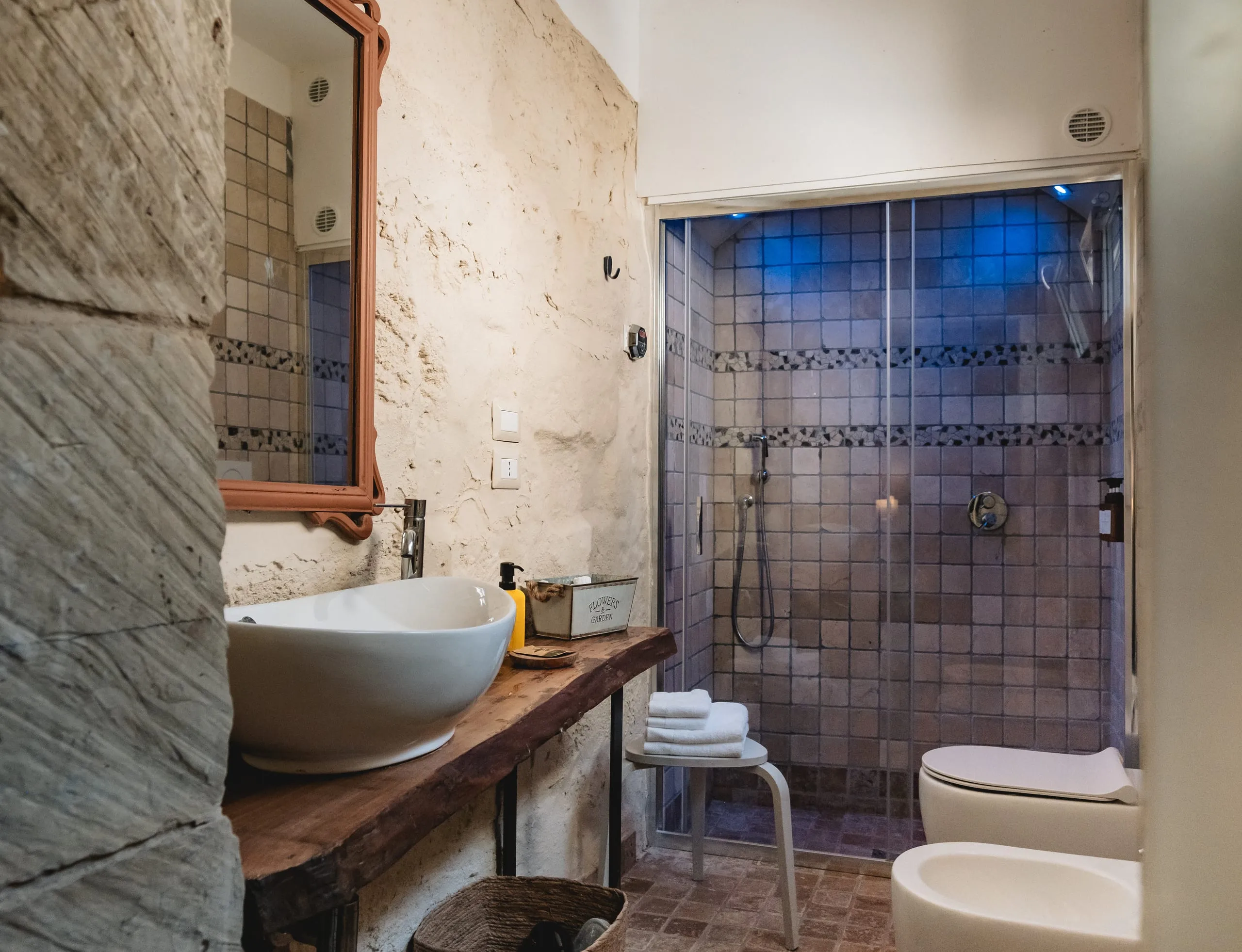Il bagno di Sciakuddhi: il lavabo in ceramica sul piano di legno e il bagno turco rivestito di mosaico blu.