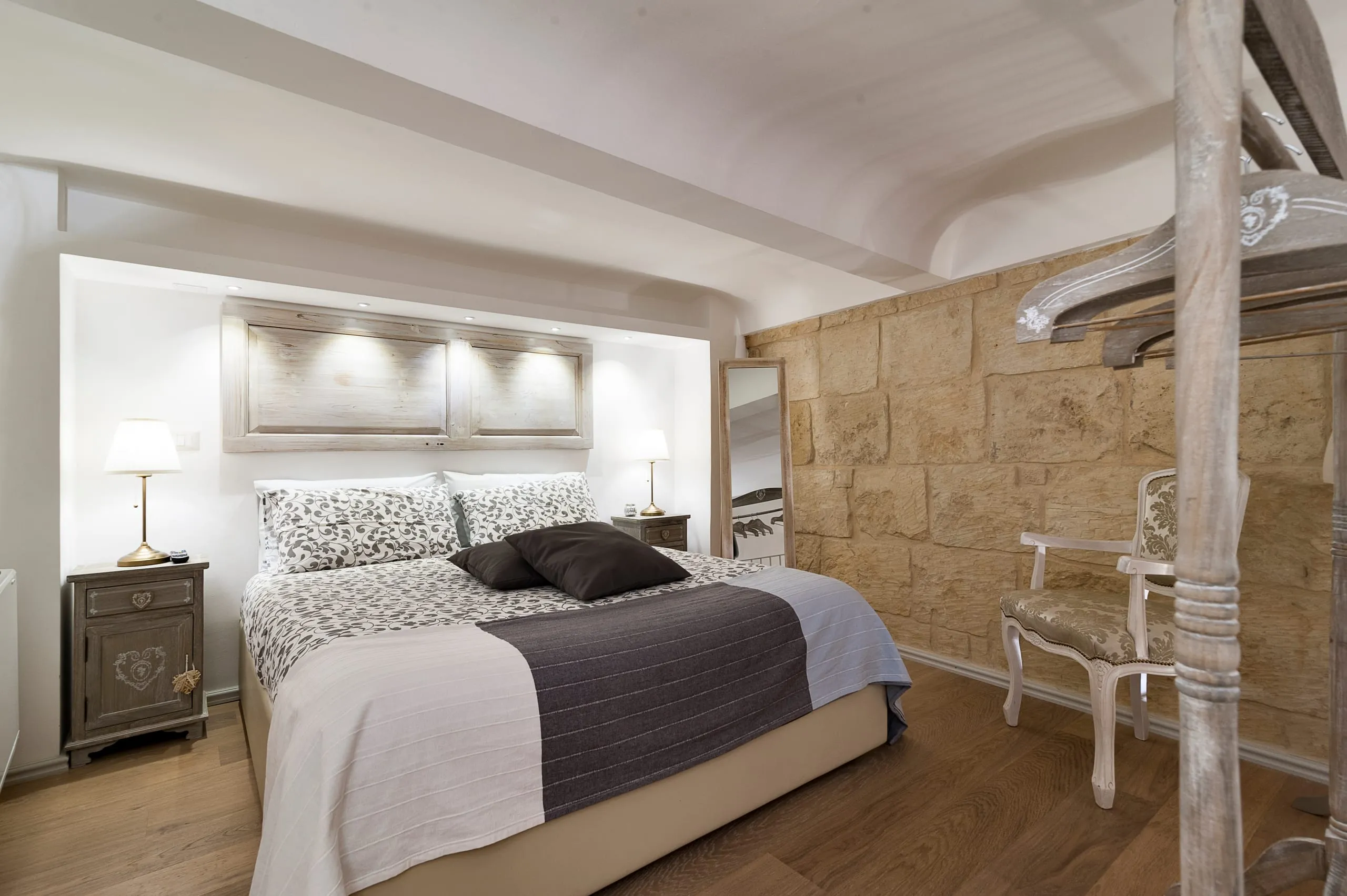 La camera della suite Sikalindi: il letto con la testiera illuminata da faretti, il pavimento di parquet, una colonna di pietra e il muro in blocchi squadrati.