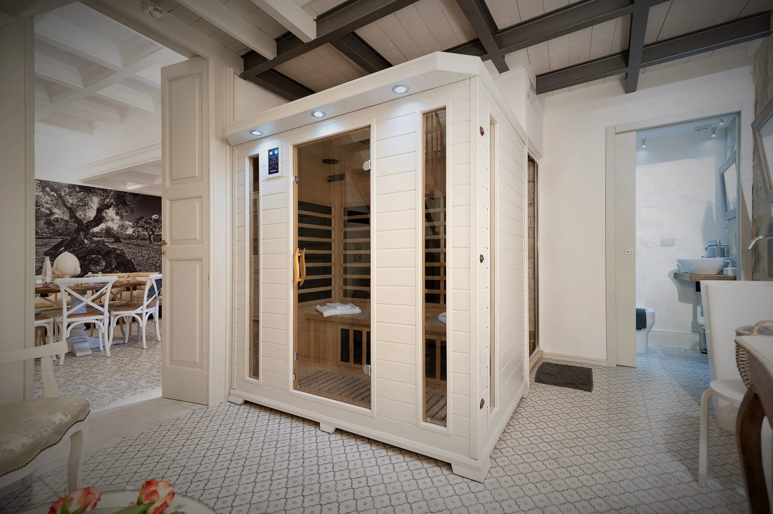 La sauna a infrarossi della suite Sikalindi: la cabina in legno chiaro sotto le travi scure, le cementine e, oltre la porta, la sala con la fotografia dell’uliveto.