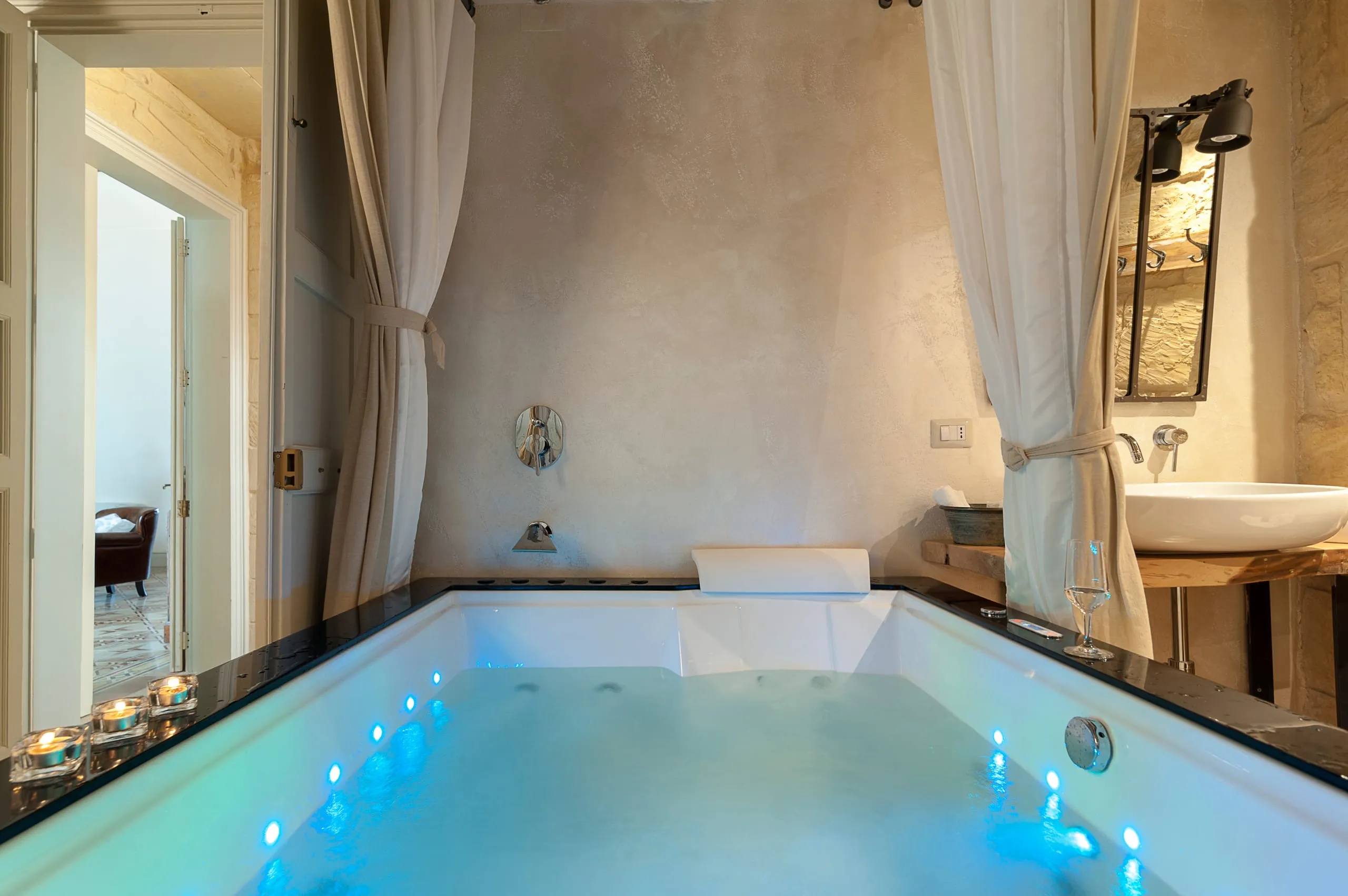 La vasca a immersione della spa, illuminata di azzurro, nella stanza a volta con le tende di lino, il lavabo di pietra e la porta che dà sulla suite.
