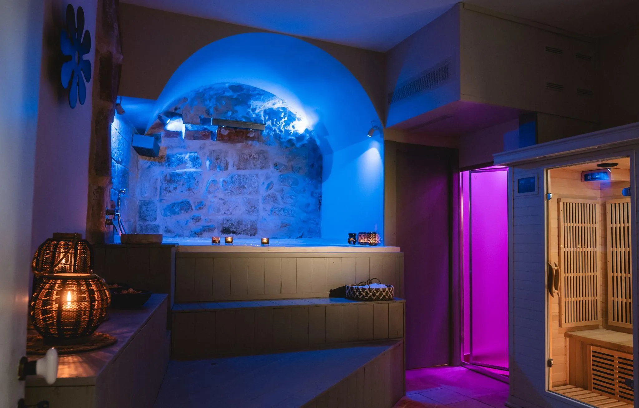 La spa di Palazzo Mandurino: la volta in pietra illuminata di blu sopra la vasca idromassaggio, il bagno turco acceso di viola e la cabina della sauna in legno.