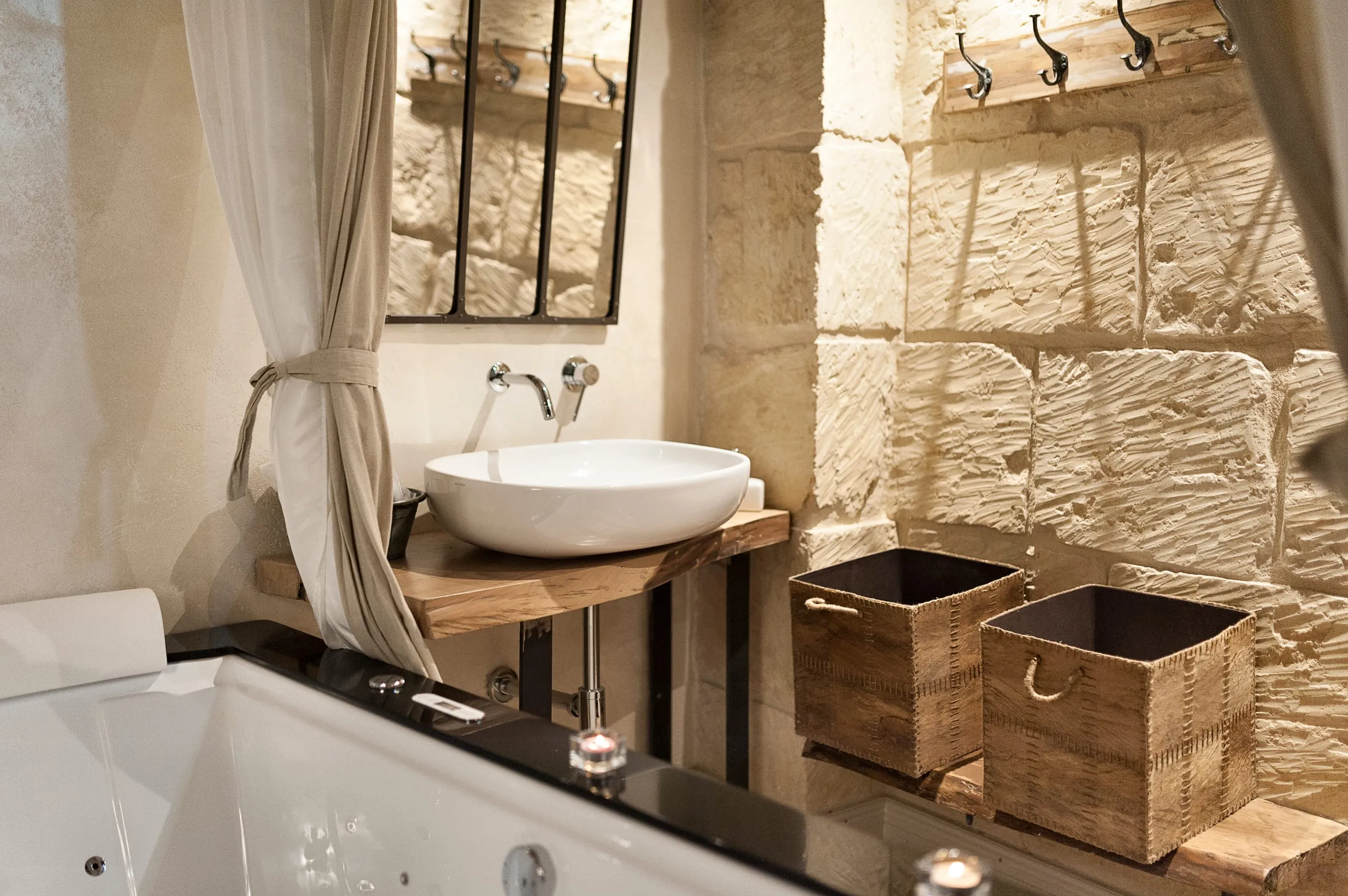 Il lavabo tondo della suite Xanti Yaca su una mensola di legno grezzo accanto alla vasca, contro il muro in blocchi di pietra chiara.