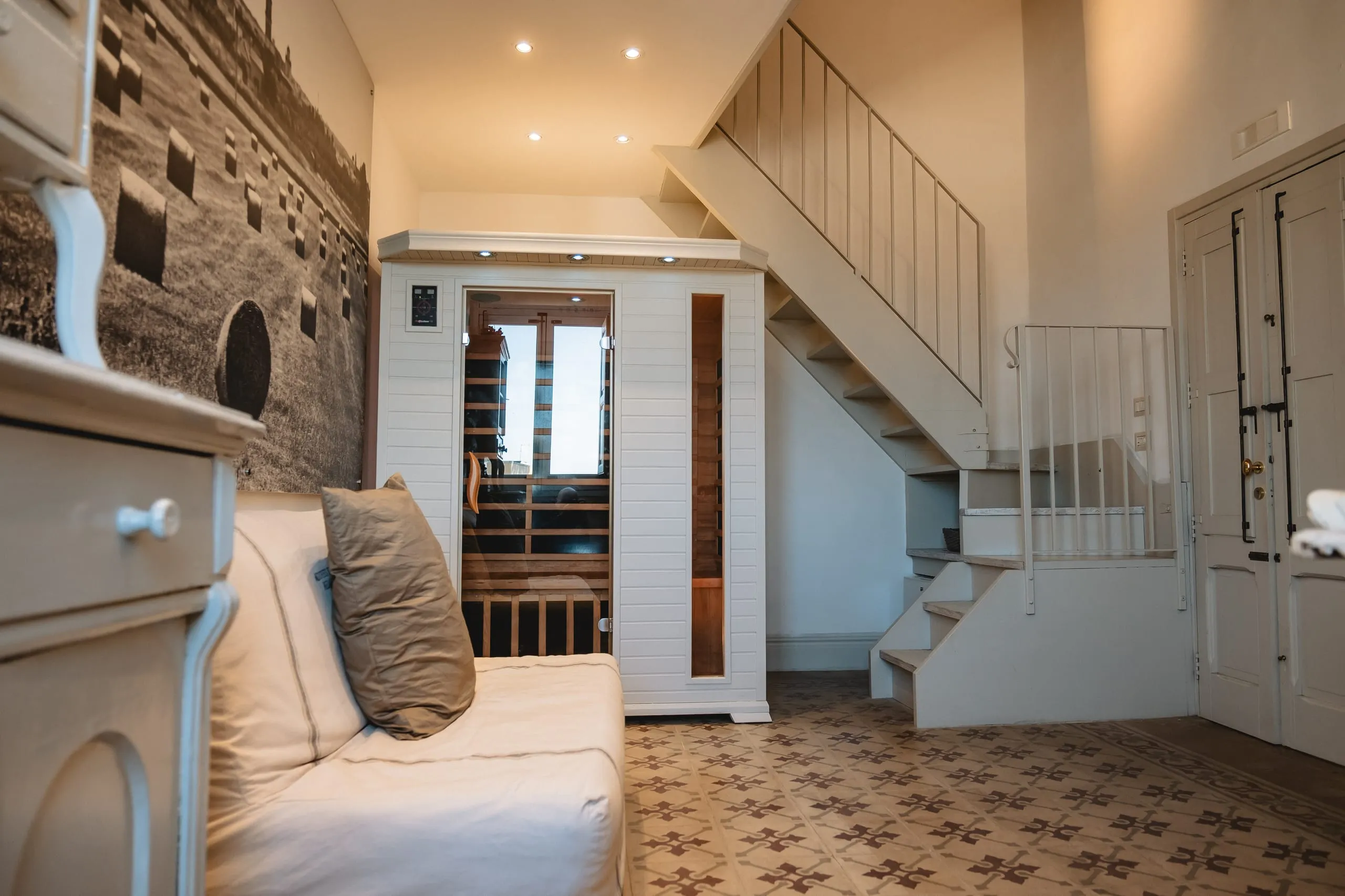 La cabina della sauna a infrarossi della suite Zagareddha, sotto la scala bianca che sale al soppalco, accanto al letto e alla fotografia delle balle di fieno.